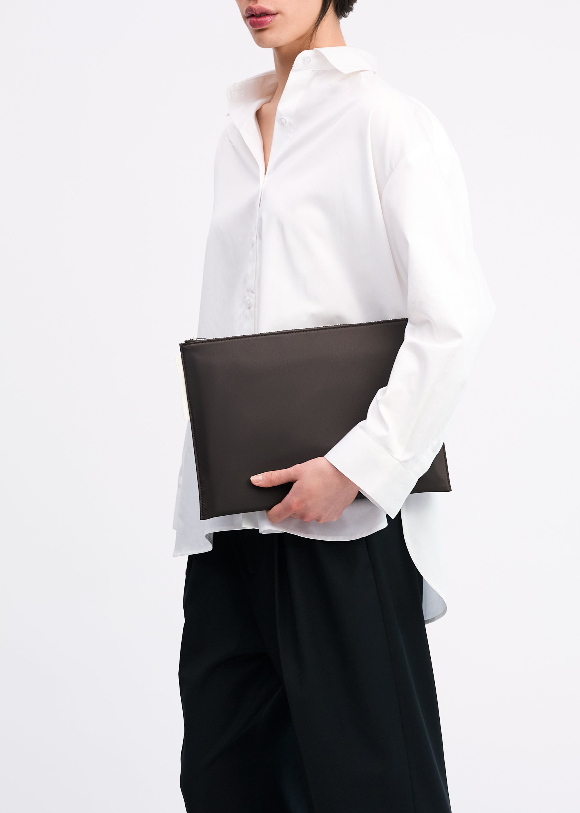 Laptop Sleeve 13" in Coffee Bean ECONYL® regenerated nylon carried in hand by model wearing white shirt and black pants