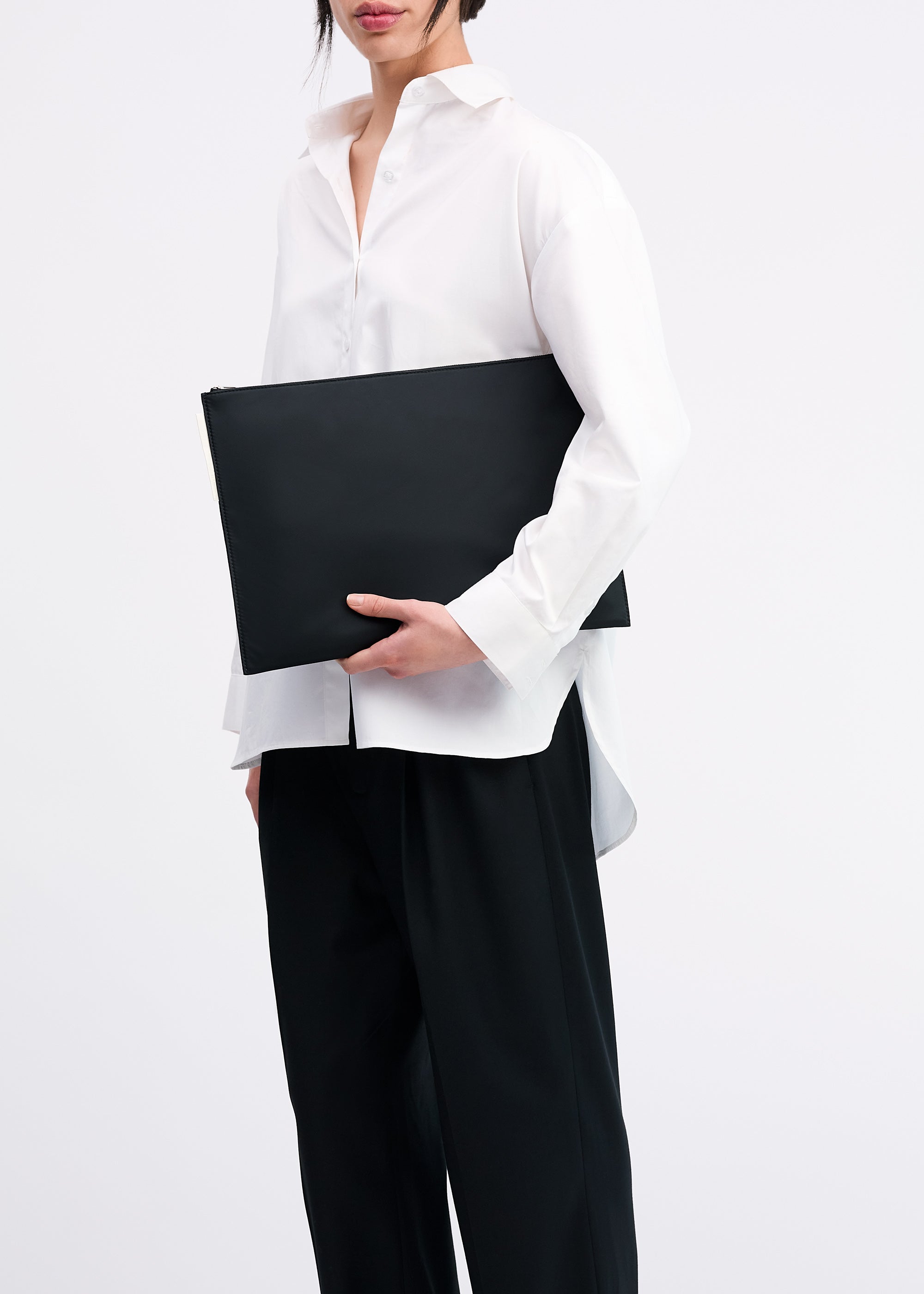 Laptop Sleeve 16" in Black ECONYL® regenerated nylon carried in hand by model wearing white shirt and black pants