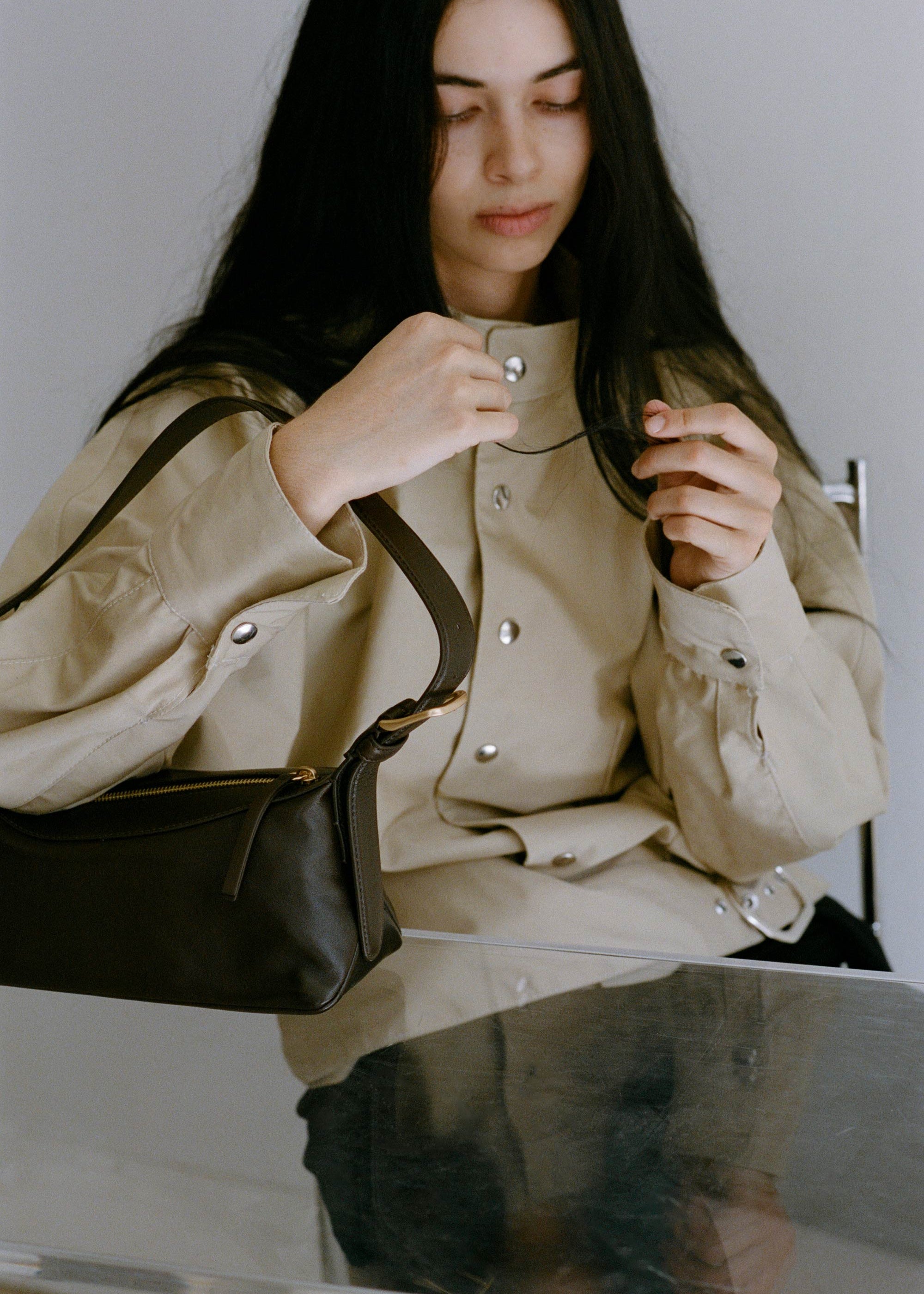 Bobby Bag in Americano Lambskin on glass table top alongside model wearing camel jacket