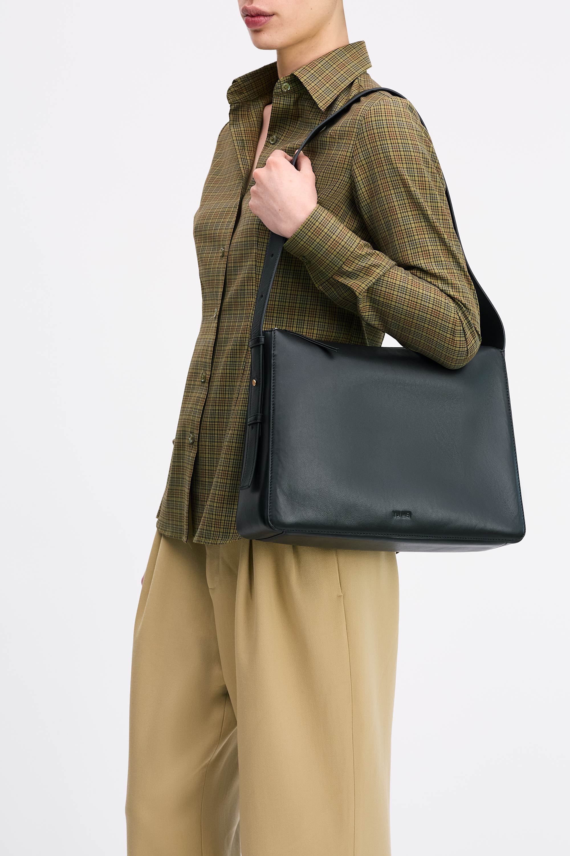 Model wearing the Charlie Bag in Black lambskin wearing a check shirt and tan pants