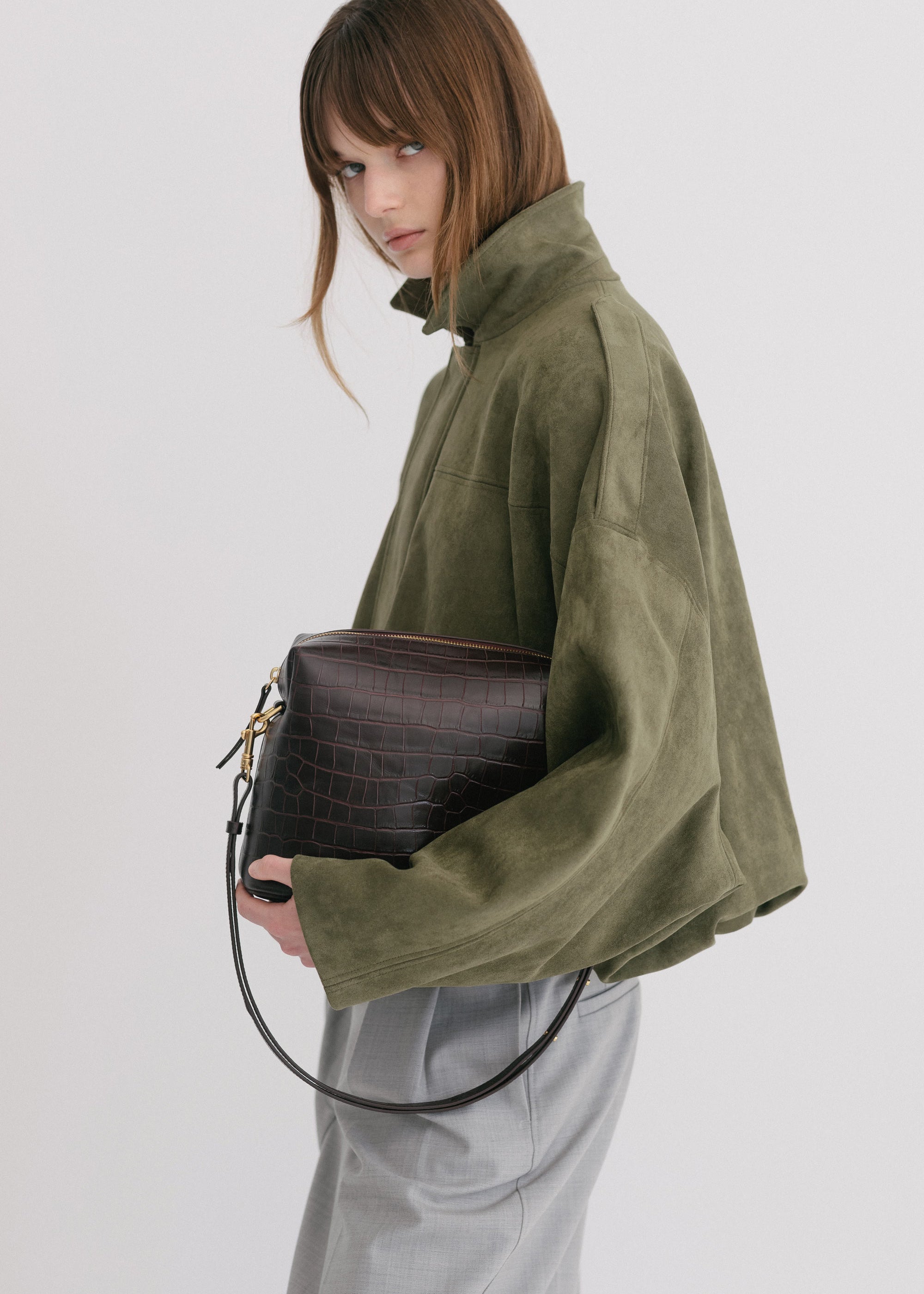 Ch'lita Bag in Fire Croc, held in models hand wearing green jacket showing detachable, adjustable strap