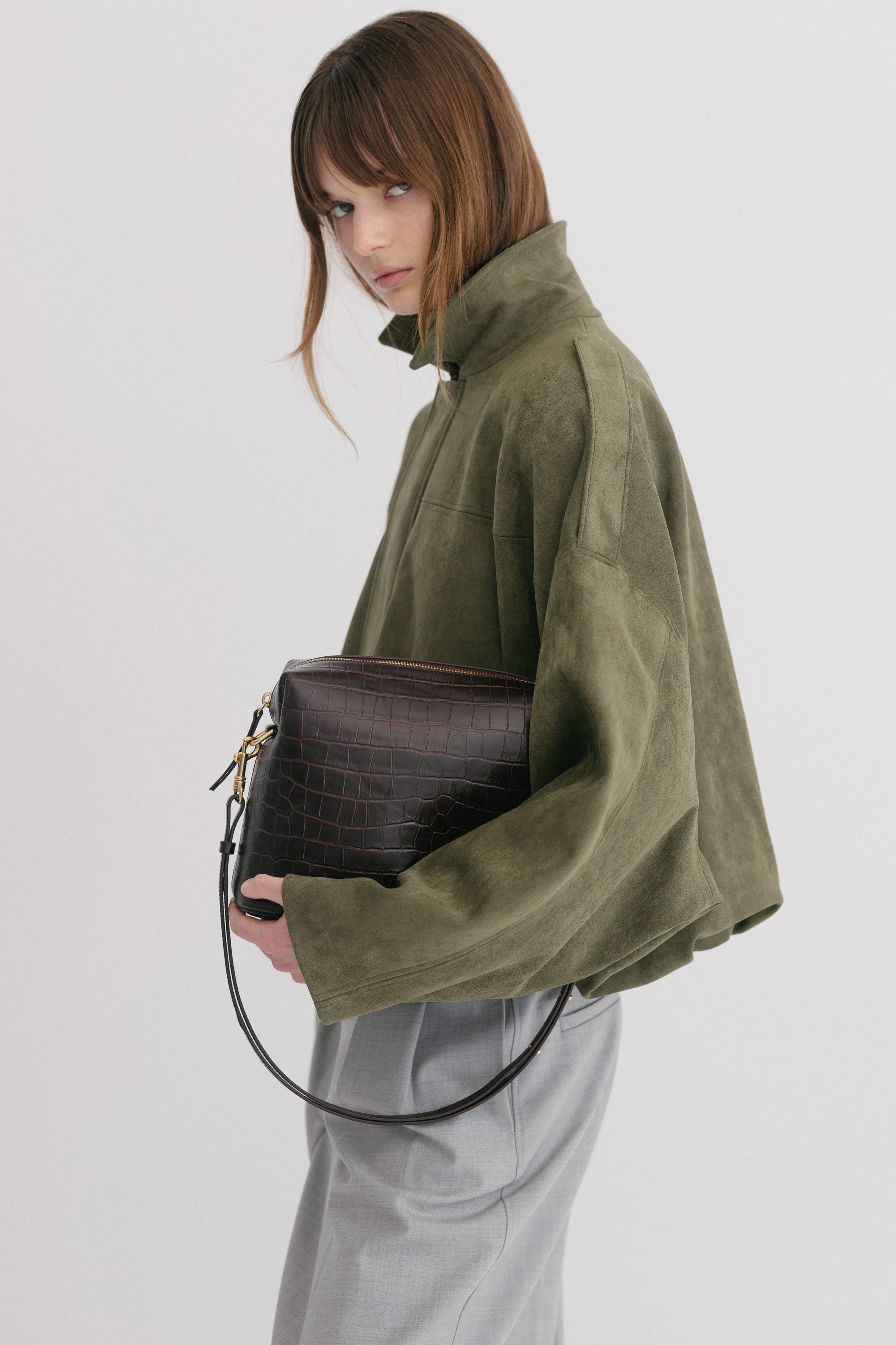 Ch'lita Bag in Fire Croc, held in models hand wearing green jacket showing detachable, adjustable strap