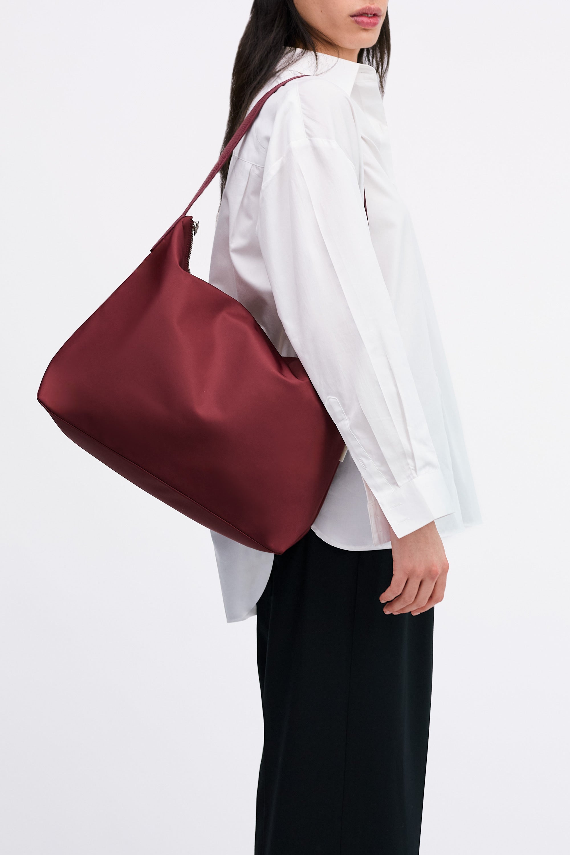 Model wearing the Medium UTILITY Braidy Bag in Pomegranate nylon on shoulder in white shirt and black trousers