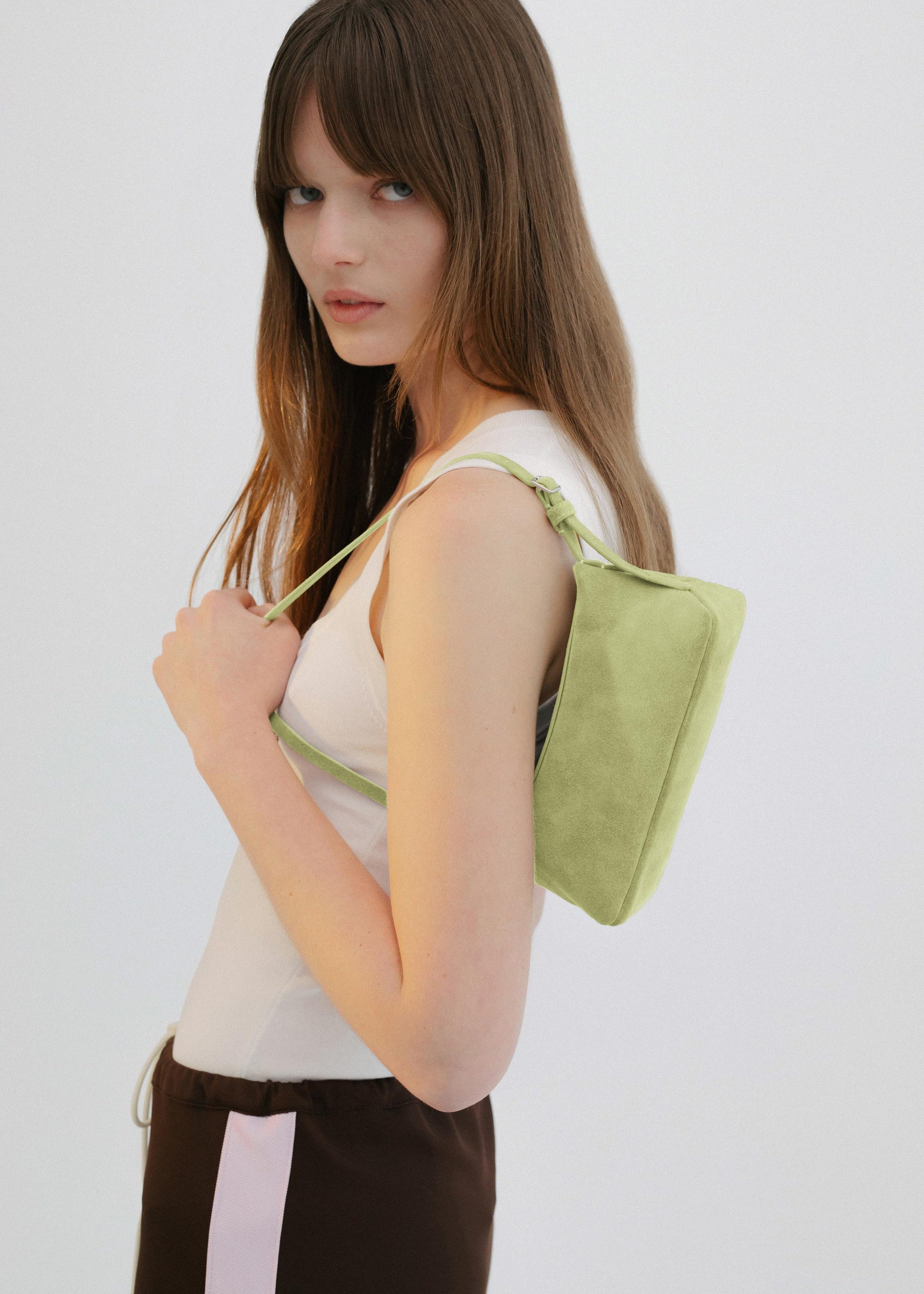 Yu Mei Mini Bobby in Apple Suede carried on shoulder of model wearing white top and brown pants.