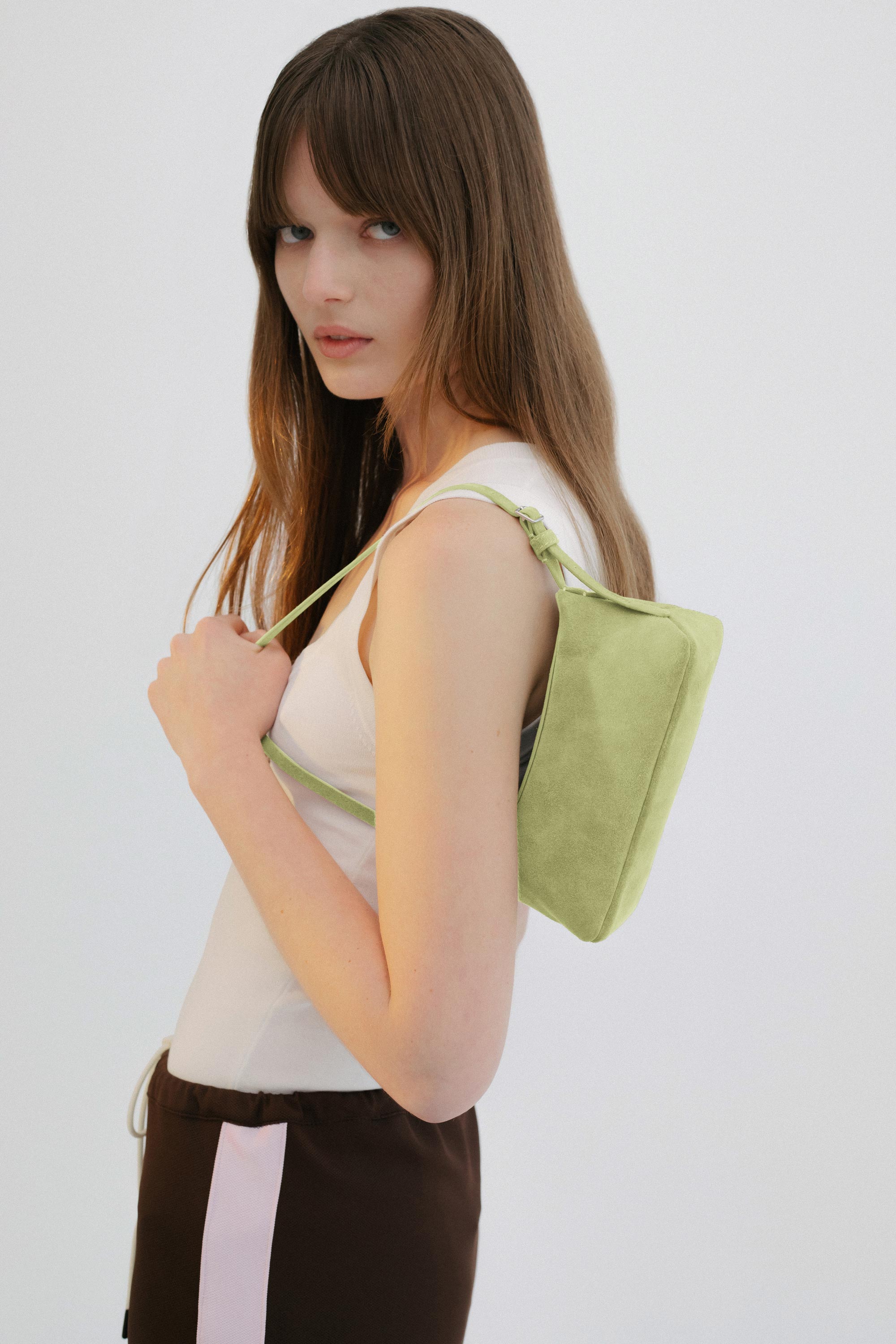 Yu Mei Mini Bobby in Apple Suede carried on shoulder of model wearing white top and brown pants.