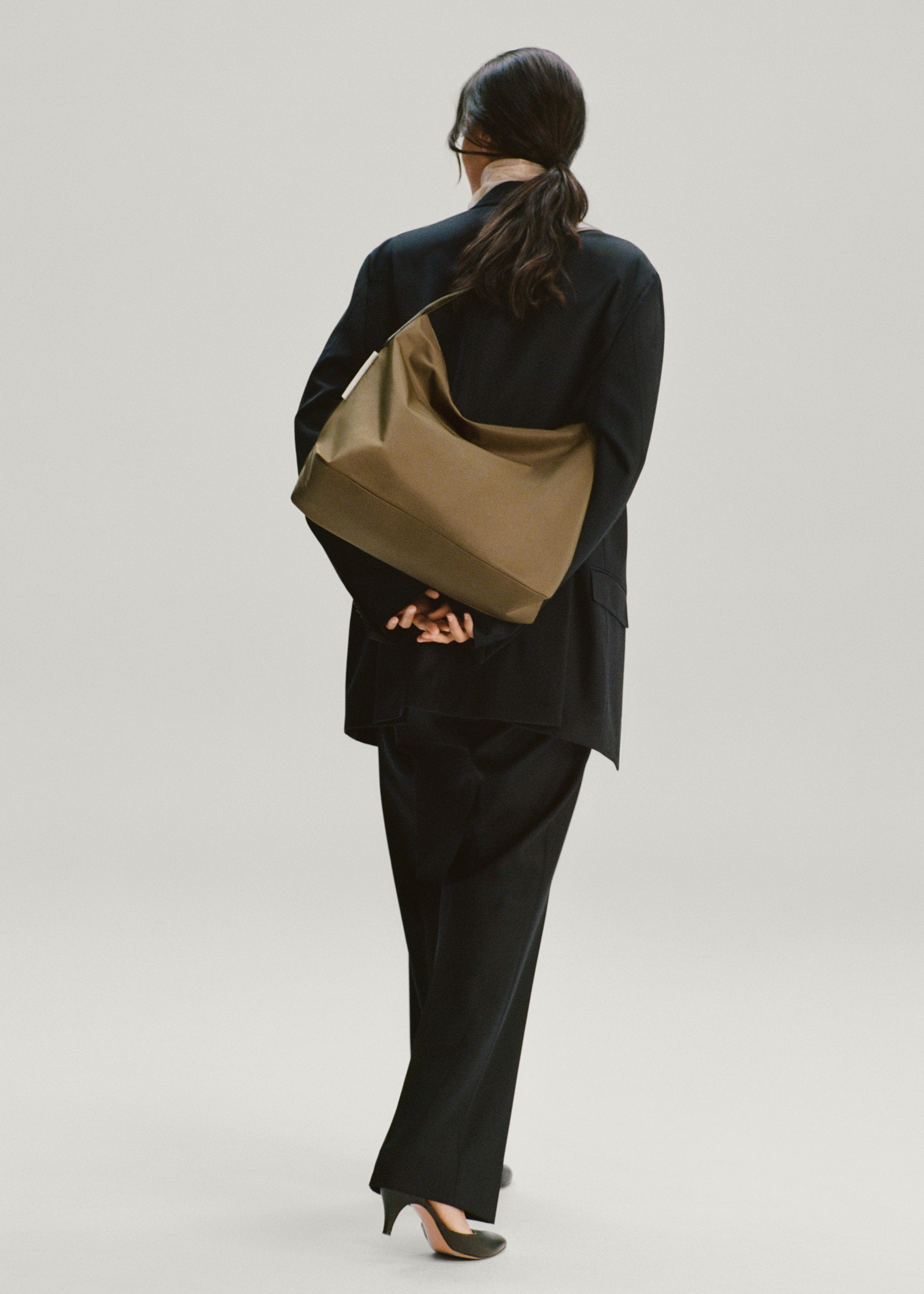 Back view of model wearing the Medium UTILITY Braidy Bag in Fir Green nylon on shoulder wearing black suit